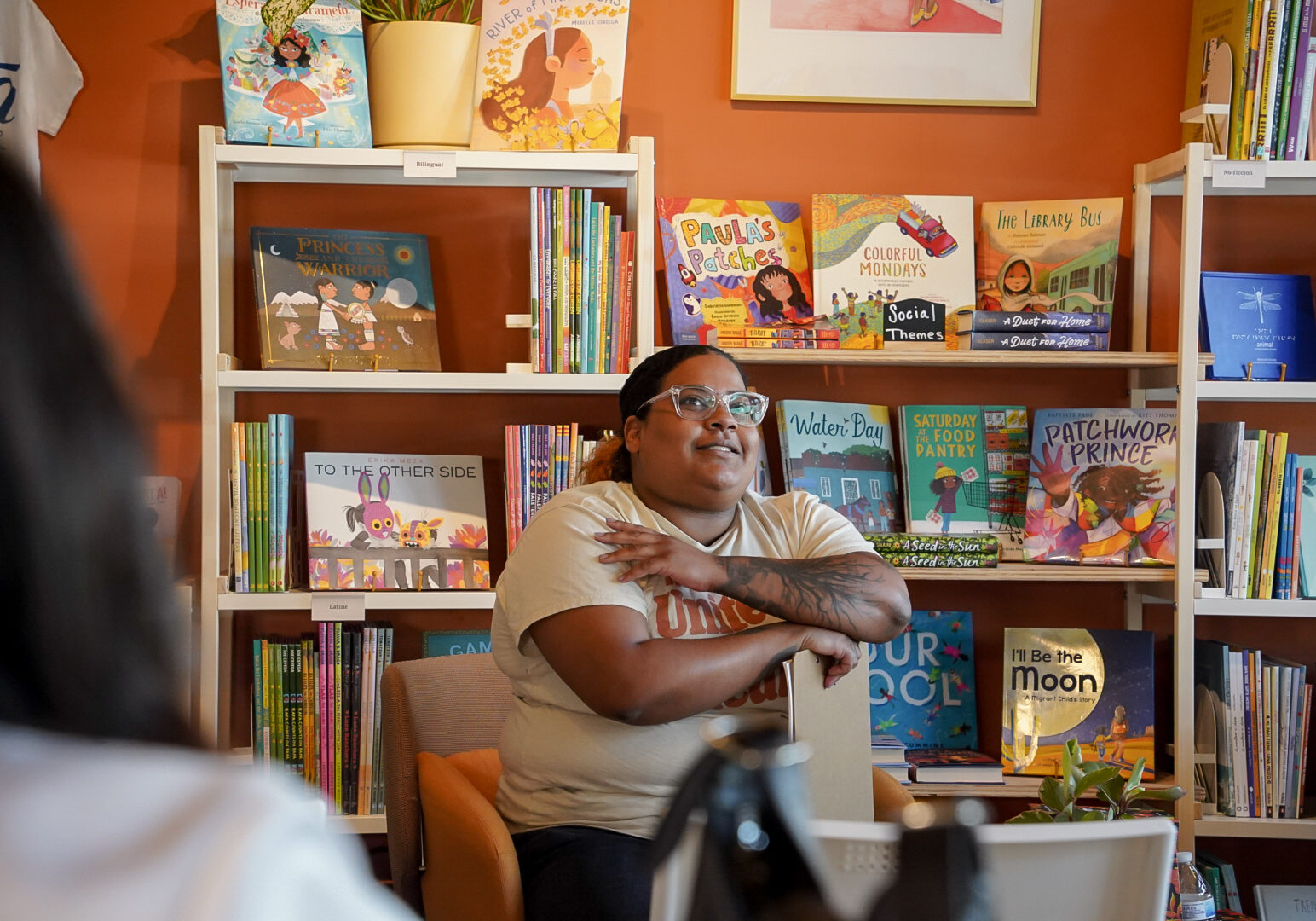 Woman sitting in chair speaking to group in front of a wall of books